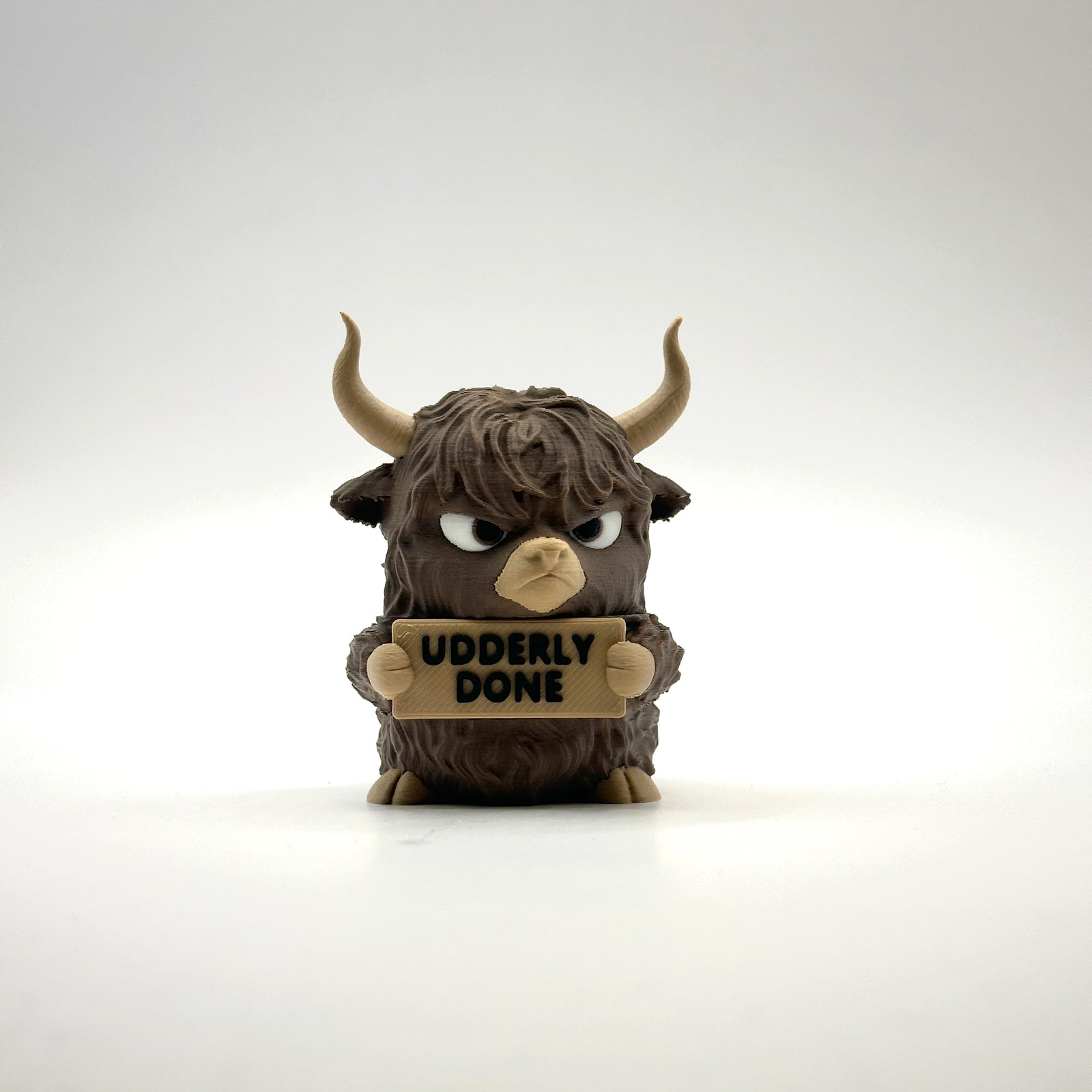 Udderly Done Highland Cow 3D printed desk buddy holding its sign, front view